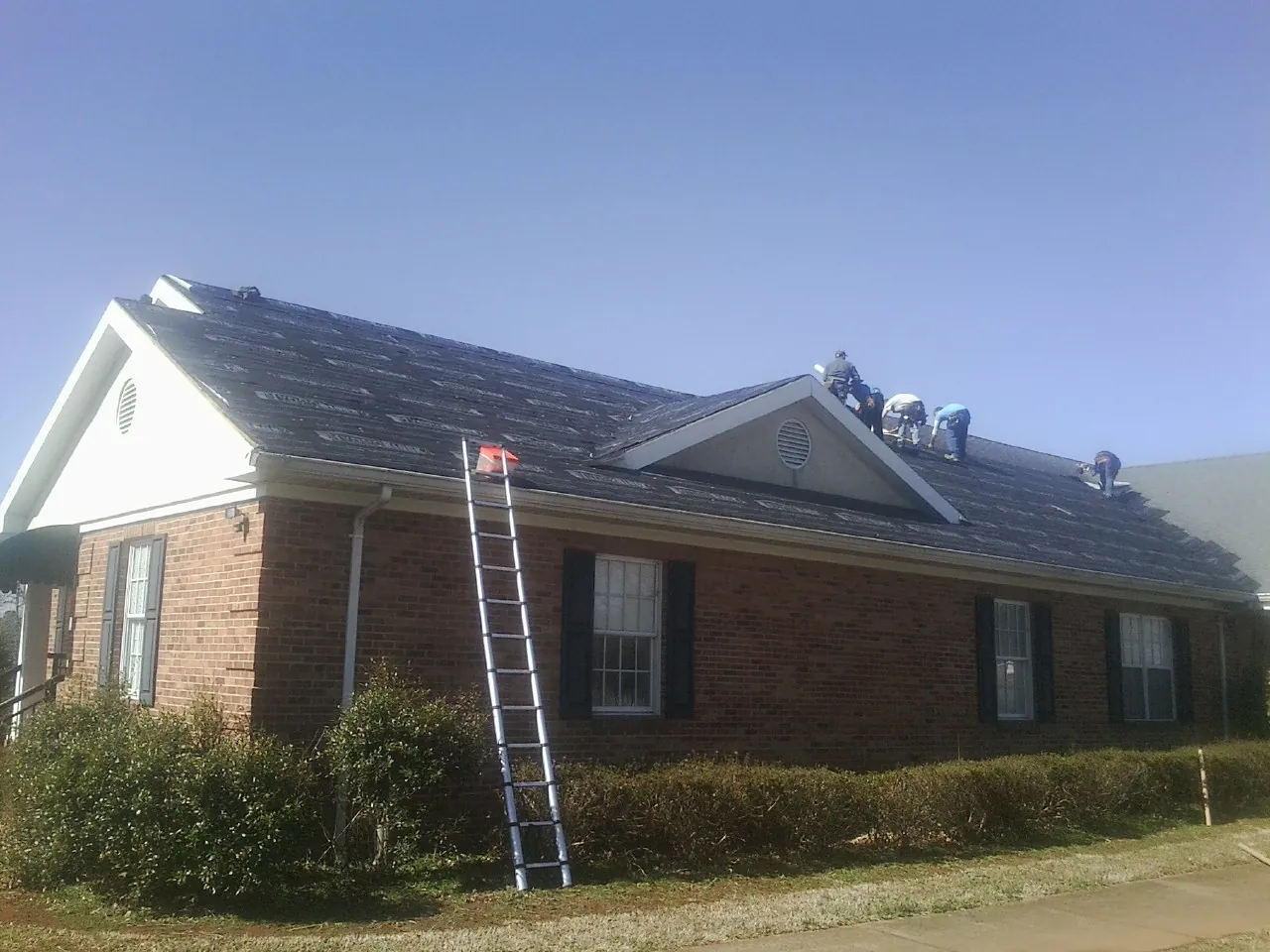 Crew tearing shingles off a brick ranch roof with a ladder set — Emergency Roof Repair work by our crew in Darlington